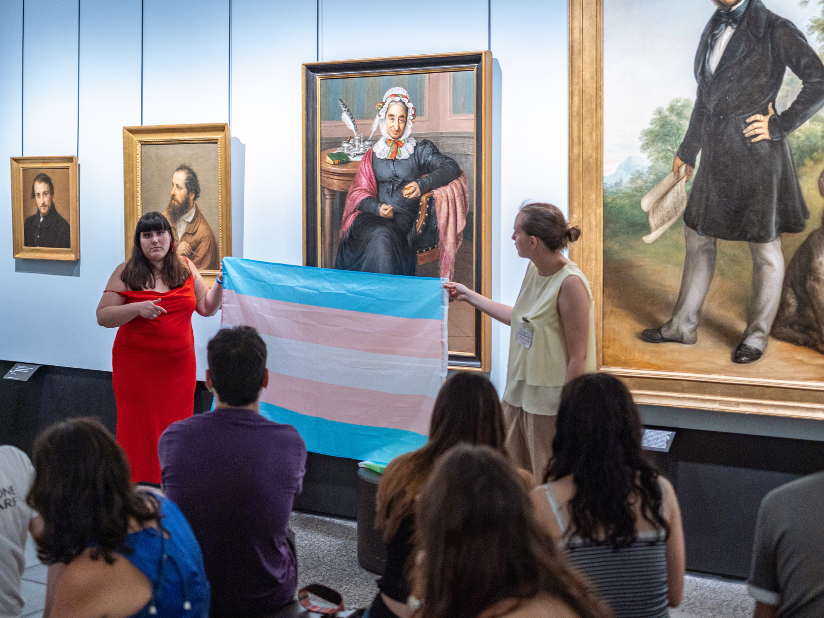 Giovani ragazzi tengono in mano la bandiera dei diritti queer nelle sale dell'accademia carrara